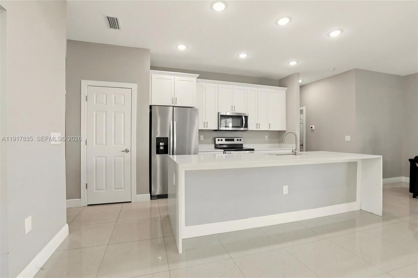 2908 9th Street Southwest Lehigh Acres, FL 33976 - Photo 12 of 44 a room with kitchen island a sink a refrigerator and cabinets
