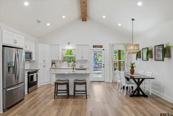 a kitchen with stainless steel appliances a dining table chairs stove refrigerator and cabinets