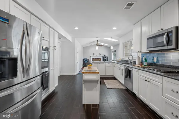 a kitchen with stainless steel appliances granite countertop a refrigerator a sink dishwasher a stove and white cabinets with wooden floor