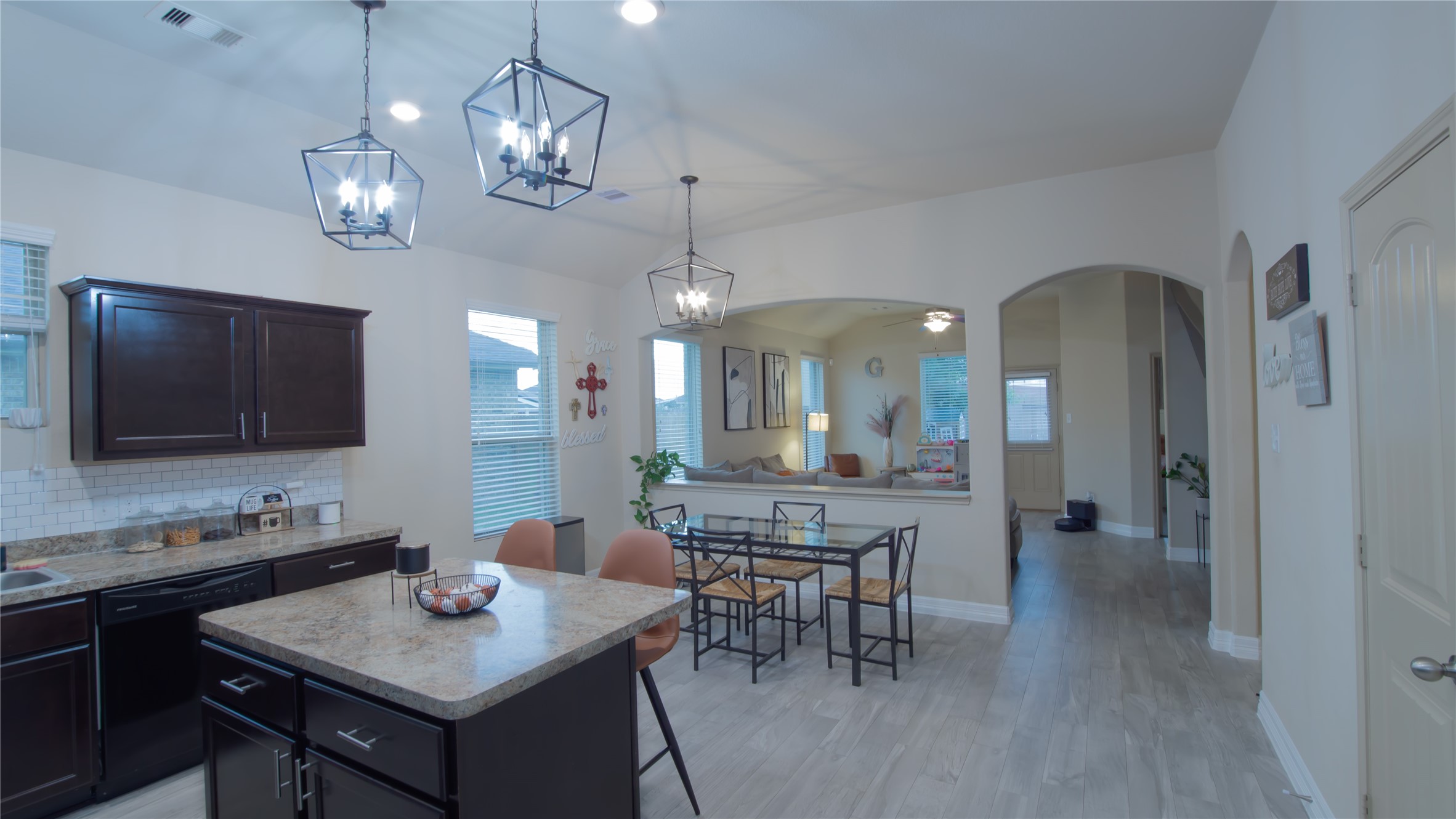 20511 Rimini River Way Katy, TX 77449 - Photo 3 of 30 Showcasing a modern open-concept layout, this kitchen and dining area features rich dark cabinetry, light countertops, and elegant pendant lighting. The dining space flows seamlessly into the inviting living area, and light wood flooring adds warmth and brightness to the entire space.