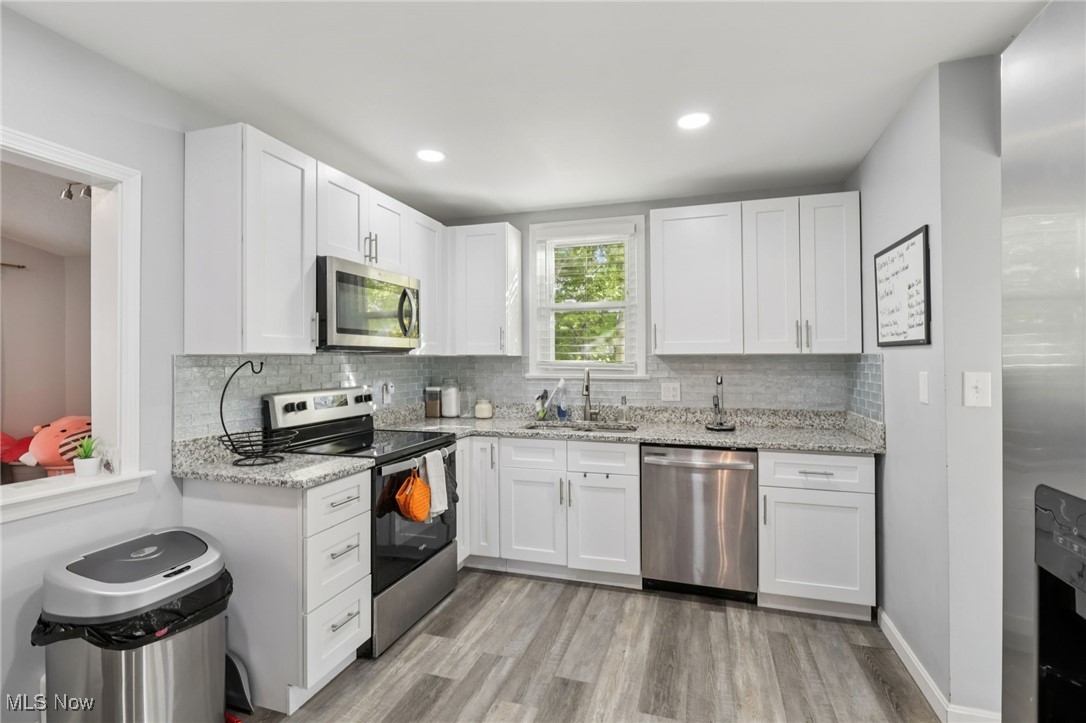 1503 Oakmount Road South Euclid, OH 44121 - Photo 20 of 50 Kitchen with appliances with stainless steel finishes, white cabinets, backsplash, light wood-style floors, and light stone countertops