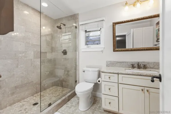 a bathroom with a granite countertop toilet a sink a mirror and shower