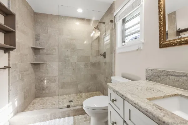 a bathroom with a granite countertop sink a toilet a mirror and shower