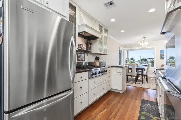 a kitchen with stainless steel appliances granite countertop a refrigerator a sink dishwasher a stove and white cabinets with wooden floor