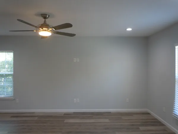 a view of an empty room with wooden floor and fan