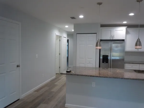 an empty room with wooden floor and a kitchen view