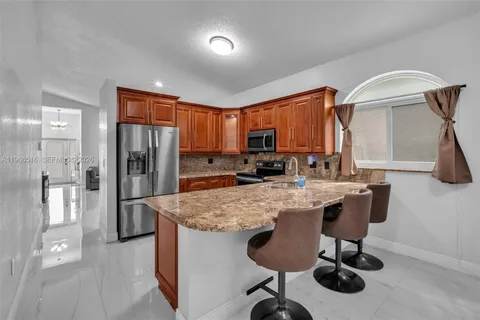 a kitchen with stainless steel appliances granite countertop a refrigerator a sink dishwasher a stove a dining table and chairs with wooden floor