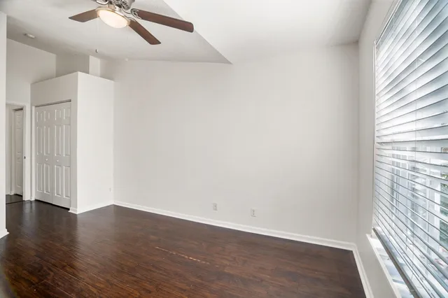 an empty room with wooden floor chandelier fan and windows