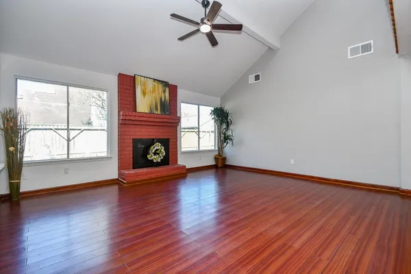 an empty room with wooden floor fireplace and windows