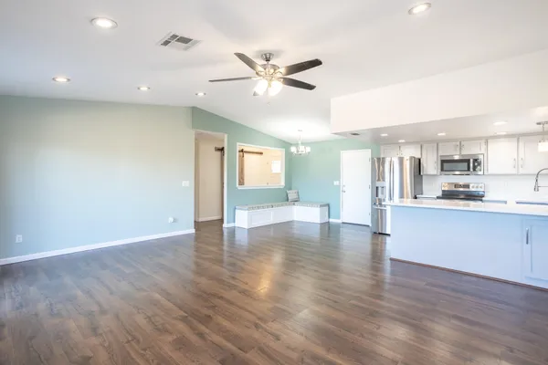 a view of an empty room and kitchen with wooden floor and fan