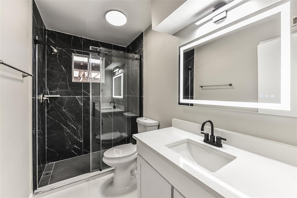 a bathroom with a shower sink vanity mirror and toilet