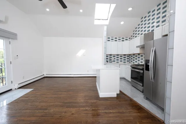 a view of a refrigerator in kitchen and an empty room with wooden floor
