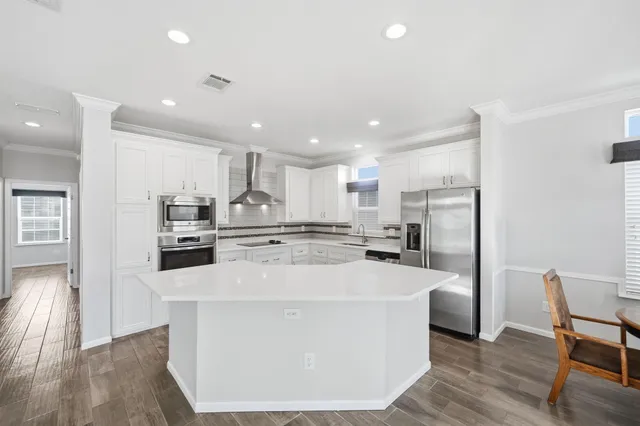 a large kitchen with stainless steel appliances a large counter top and wooden floors