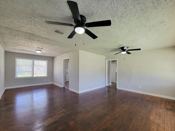 an empty room with wooden floor chandelier fan and windows
