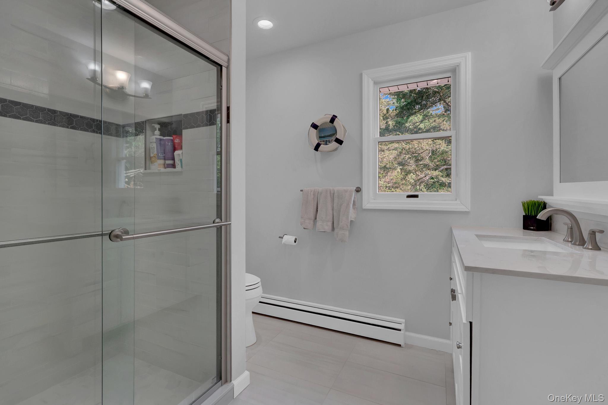 15 Stillwater Road Nissequogue, NY 11780 - Photo 25 of 43 Bathroom featuring a glass-enclosed shower with tile surround and hexagon accent, single vanity with integrated sink and chrome faucet, single window, and a wall-mounted mirror