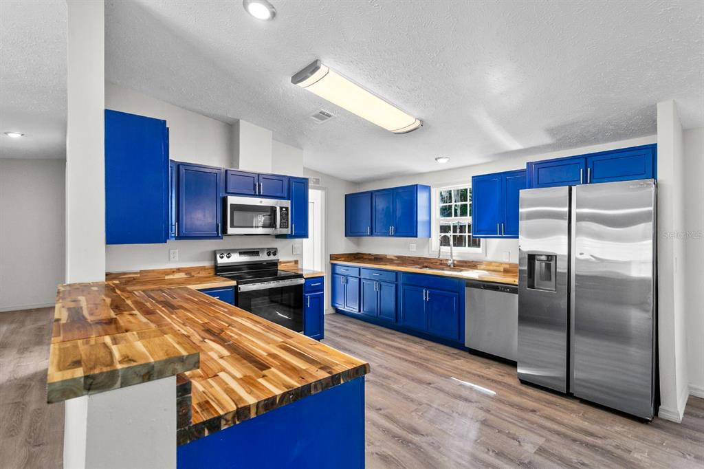 4793 Sunset Road St. Cloud, FL 34771 - Photo 8 of 28 a kitchen with stainless steel appliances granite countertop a refrigerator a stove top oven a sink dishwasher and wooden cabinets with wooden floor