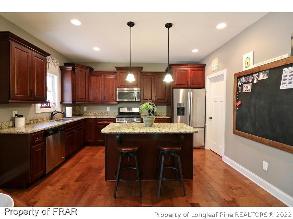 1187 Rays Bridge Road Whispering Pines, NC 28327 - Photo 29 of 35 a kitchen with stainless steel appliances granite countertop a sink a stove a refrigerator and wooden floor