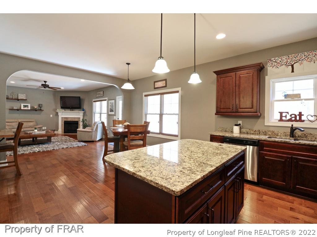1187 Rays Bridge Road Whispering Pines, NC 28327 - Photo 30 of 35 a kitchen with granite countertop a stove a sink dishwasher and wooden cabinets with wooden floor