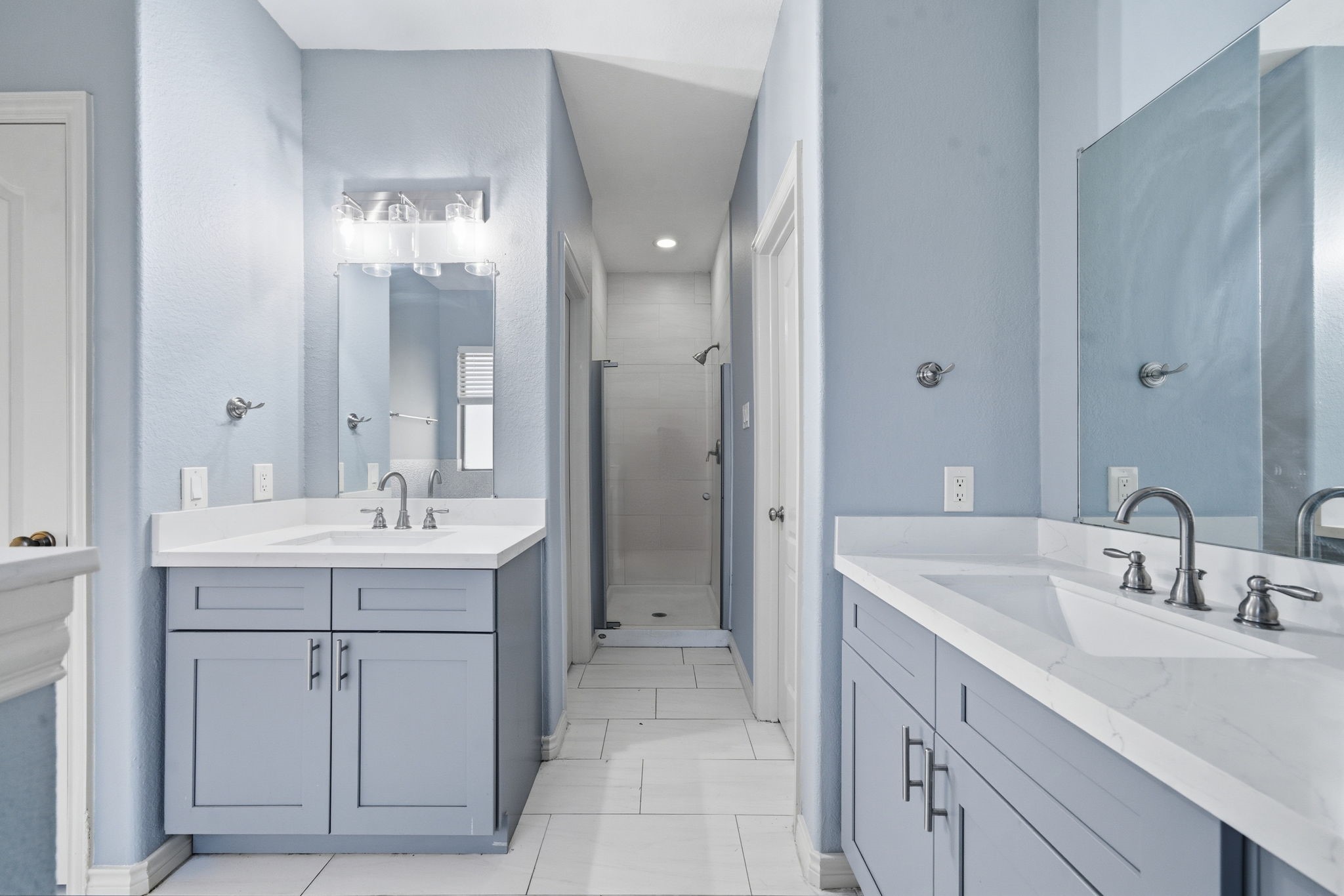 23139 Tranquil Spring Lane Katy, TX 77494 - Photo 14 of 22 Primary bathroom features dual sinks with sleek faucets on modern, light blue vanities. It has a spacious walk-in shower and is well-lit with contemporary fixtures, creating a fresh and inviting atmosphere.