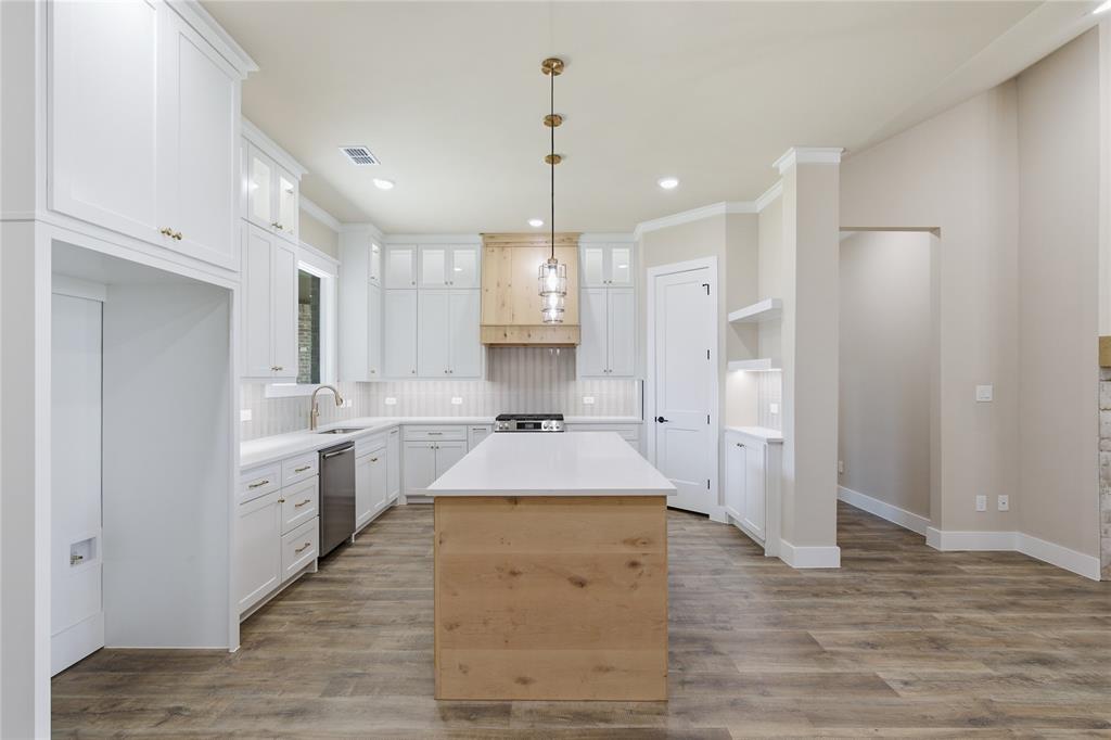 709 Anne Road Van Alstyne, TX 75495 - Photo 7 of 28 Open-concept kitchen featuring a central island with wood-finish paneling, white cabinetry, and light-toned countertops