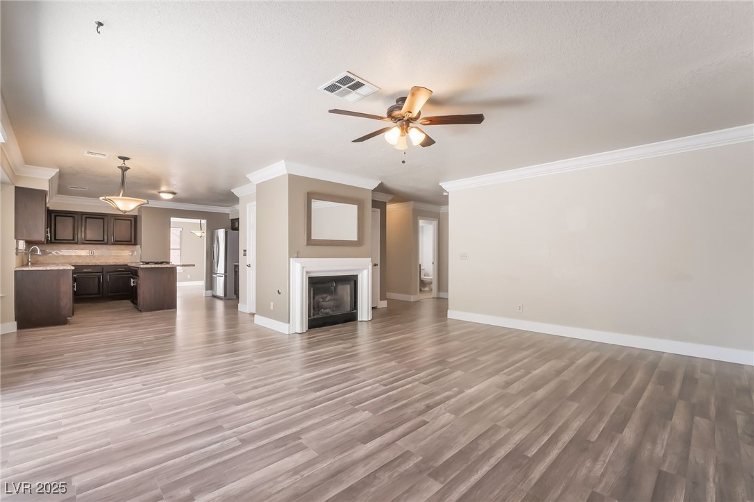 1804 Michaels Court Henderson, NV 89014 - Photo 11 of 44 Unfurnished living room with a ceiling fan, crown molding, light wood-style flooring, and a fireplace