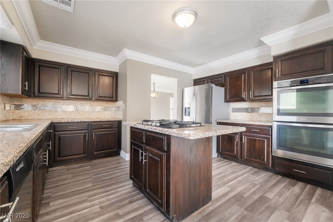 1804 Michaels Court Henderson, NV 89014 - Photo 6 of 44 Kitchen with appliances with stainless steel finishes, light wood-style floors, dark brown cabinets, and ornamental molding