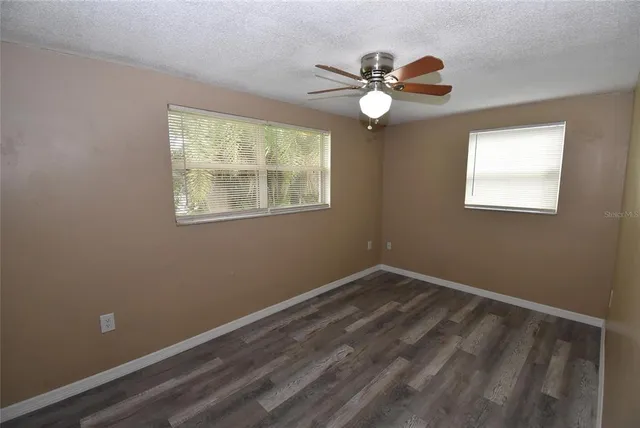an empty room with wooden floor fan and windows