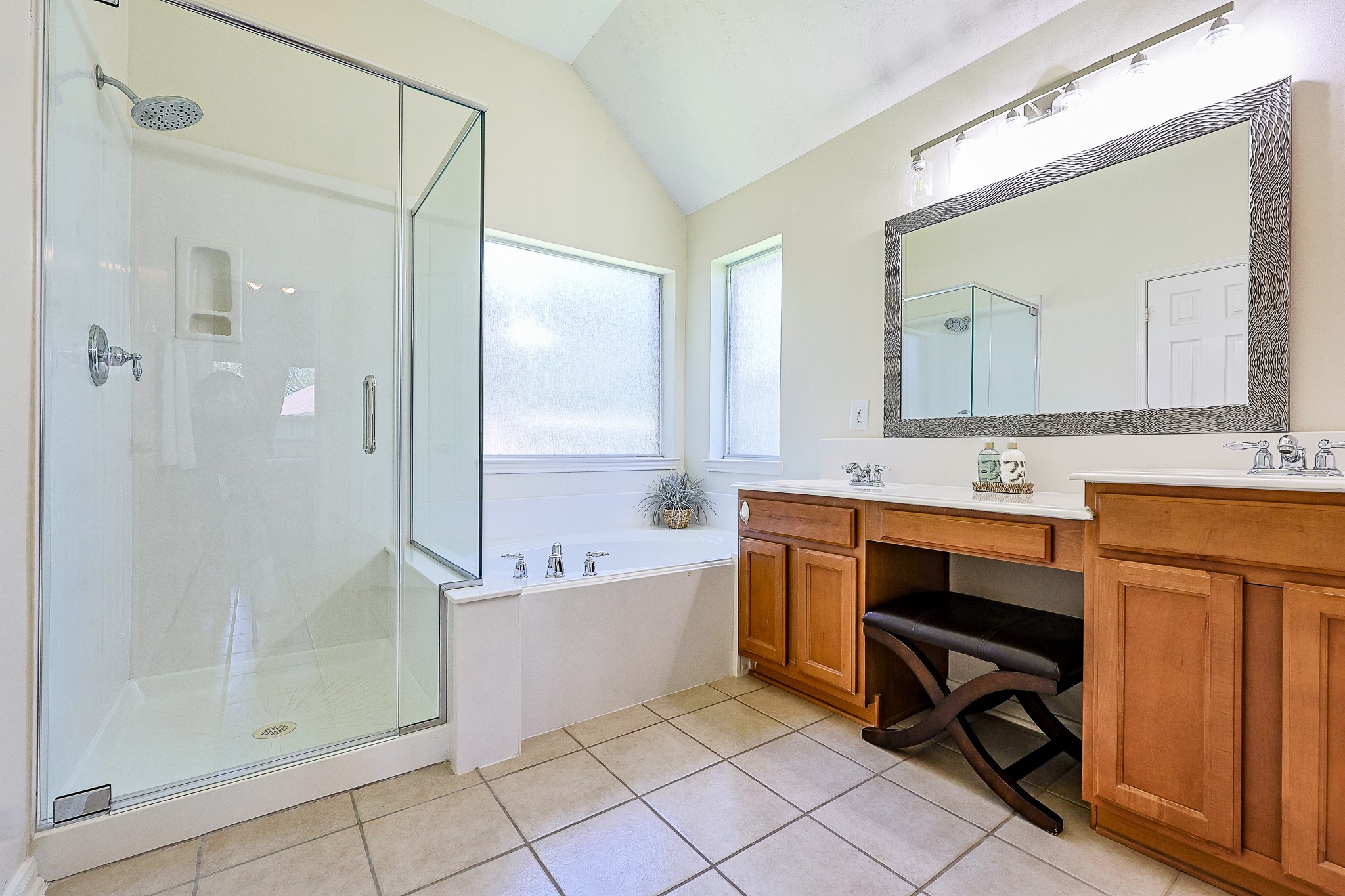 10306 Rudolph Court Missouri City, TX 77459 - Photo 18 of 34 Indulge in your own private oasis with this beautifully designed primary bathroom, offering a perfect blend of luxury, storage and modern amenities. Features a pristine, modern walk-in shower enclosed in semi frameless glass, large soaking tub, maple wood vanity cabinetry with knee space and oversized framed mirror. Complemented by high ceiling, tile flooring and rain glass corner windows for privacy.