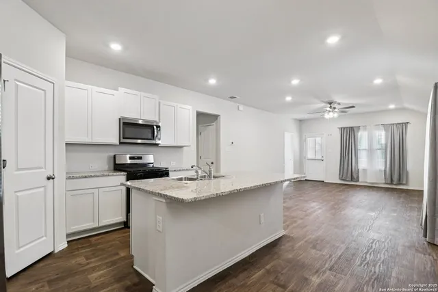 a kitchen with stainless steel appliances kitchen island granite countertop a stove a sink and white cabinets with wooden floor