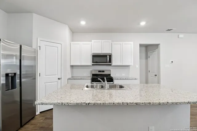 a kitchen with granite countertop a refrigerator a sink and white cabinets