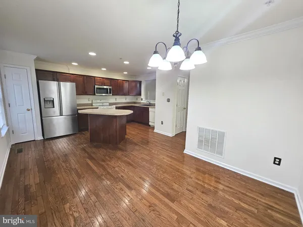 a open kitchen with stainless steel appliances granite countertop a sink a microwave oven a refrigerator and white cabinets with wooden floor