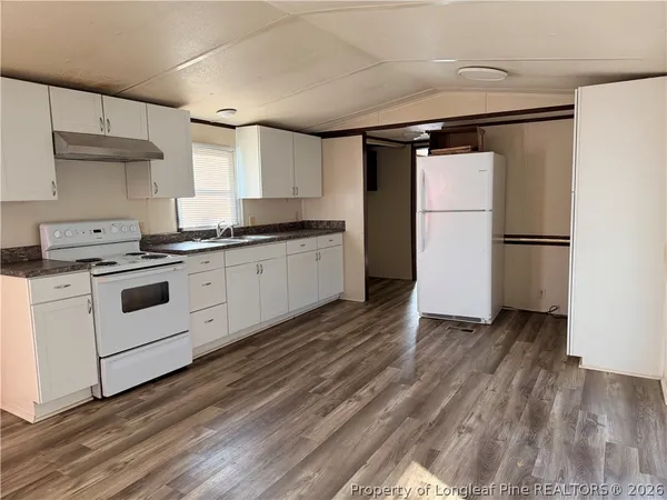 a kitchen with granite countertop a refrigerator a sink dishwasher a stove and white cabinets with wooden floor