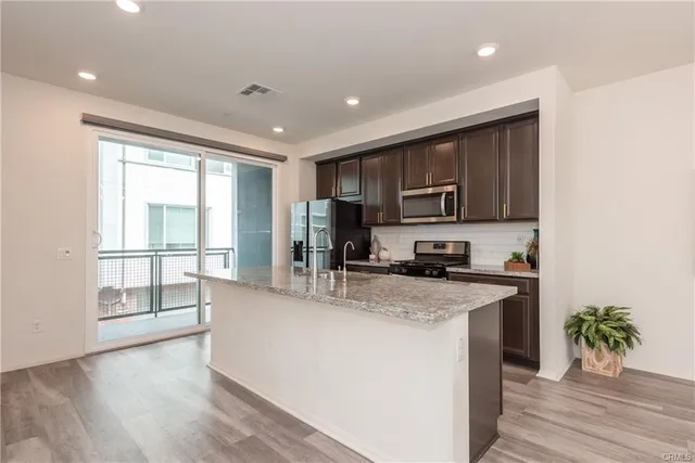 a kitchen with stainless steel appliances granite countertop a refrigerator a stove top oven a sink and dishwasher with wooden floor