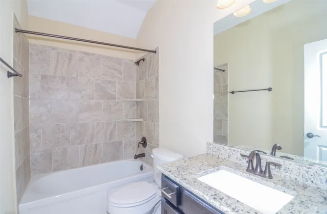 a bathroom with a granite countertop bathtub shower sink vanity and toilet