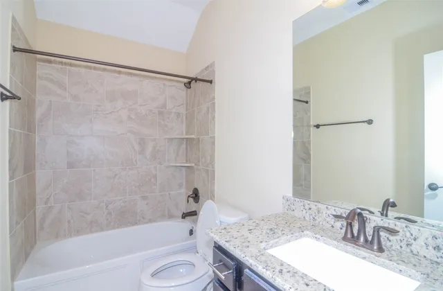 a bathroom with a granite countertop bathtub shower sink vanity and a toilet