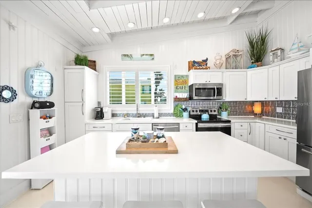 a living room with stainless steel appliances a white table and chairs in it