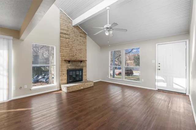 a view of an empty room with wooden floor fireplace and a window