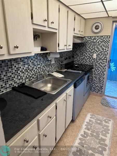 a kitchen with granite countertop a sink dishwasher a stove and white cabinets