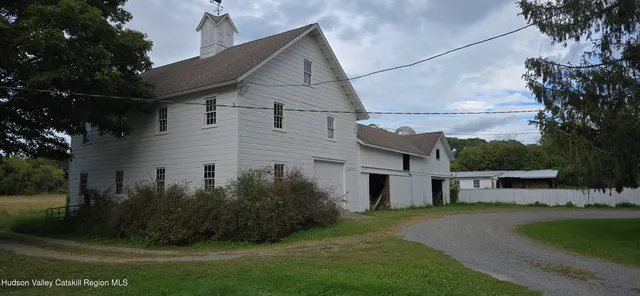 a view of a white house next to a yard with large trees