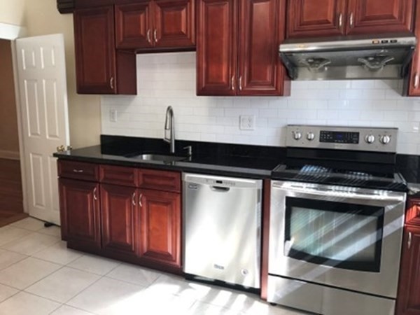 139 Pine Street, Unit 1/F Quincy, MA 02170 - Photo 4 of 10 a kitchen with granite countertop wood cabinets and stainless steel appliances