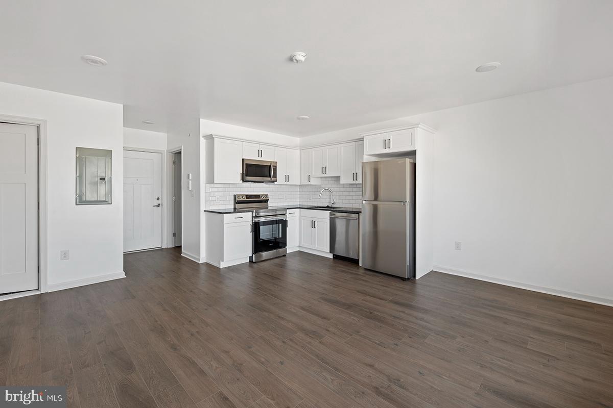 404 Fountain Street, Unit 208 Philadelphia, PA 19128 - Photo 5 of 8 a view of a kitchen with a refrigerator a stove top oven and white cabinets with wooden floor