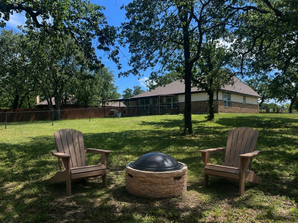 420 Sessums Road Springtown, TX 76082 - Photo 35 of 40 Expansive grassy yard featuring mature trees and a stone-clad fire pit with a protective cover -virtually staged