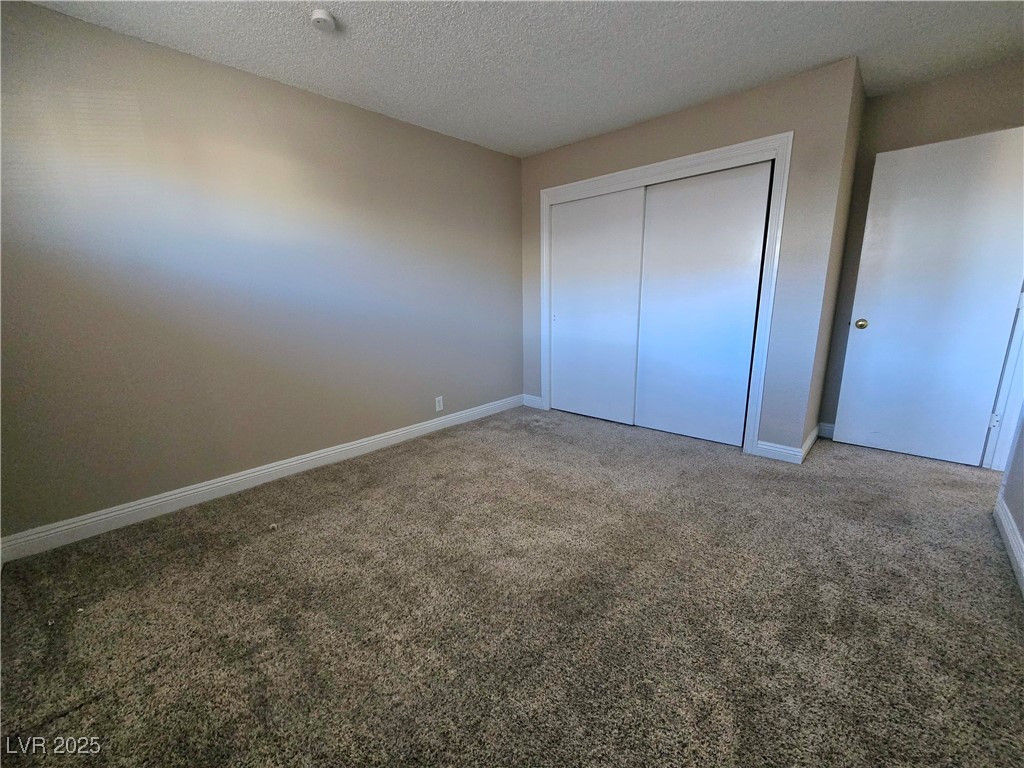 5248 Pebble Beach Boulevard, Unit D Las Vegas, NV 89108 - Photo 12 of 13 Unfurnished bedroom with a textured ceiling, carpet, and a closet