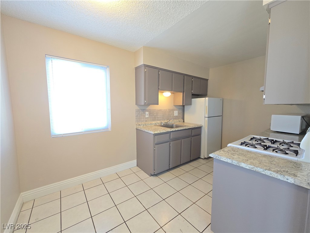 5248 Pebble Beach Boulevard, Unit D Las Vegas, NV 89108 - Photo 2 of 13 Kitchen with light countertops, tasteful backsplash, white appliances, a textured ceiling, and gray cabinetry