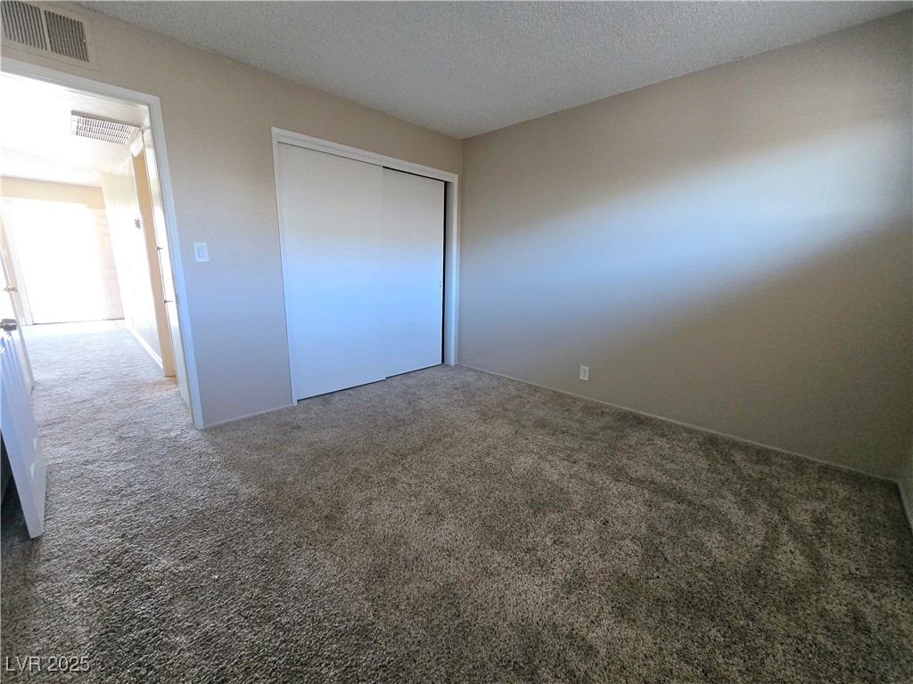 5248 Pebble Beach Boulevard, Unit D Las Vegas, NV 89108 - Photo 9 of 13 Unfurnished bedroom with carpet, a textured ceiling, and a closet