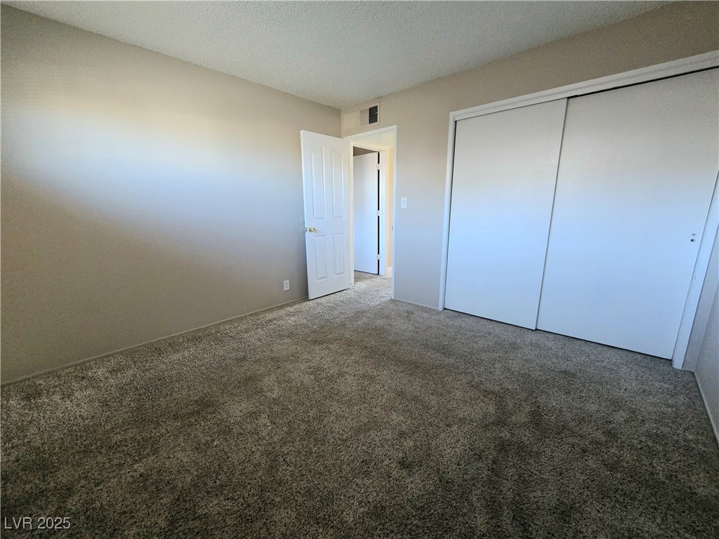 5248 Pebble Beach Boulevard, Unit D Las Vegas, NV 89108 - Photo 10 of 13 Unfurnished bedroom featuring carpet flooring, a closet, and a textured ceiling
