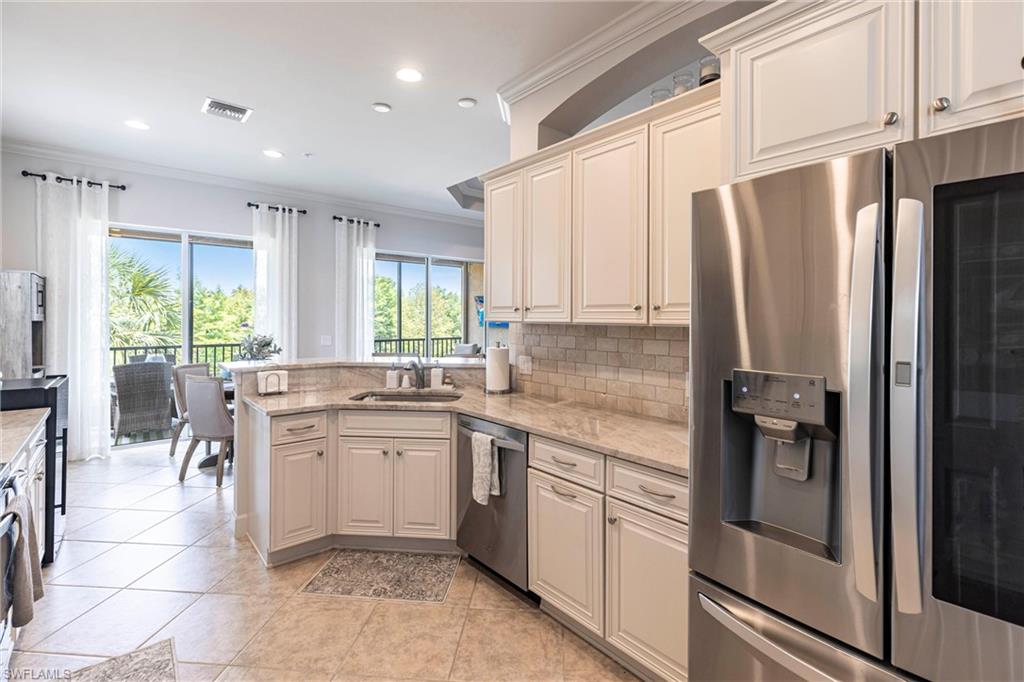 9550 Ironstone Terrace, Unit 201 Naples, FL 34120 - Photo 12 of 50 Kitchen featuring appliances with stainless steel finishes, a sink, crown molding, a peninsula, and backsplash