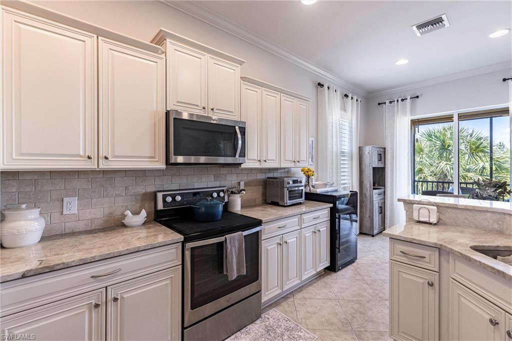 9550 Ironstone Terrace, Unit 201 Naples, FL 34120 - Photo 17 of 50 Kitchen with appliances with stainless steel finishes, tasteful backsplash, ornamental molding, light tile patterned flooring, and light stone counters