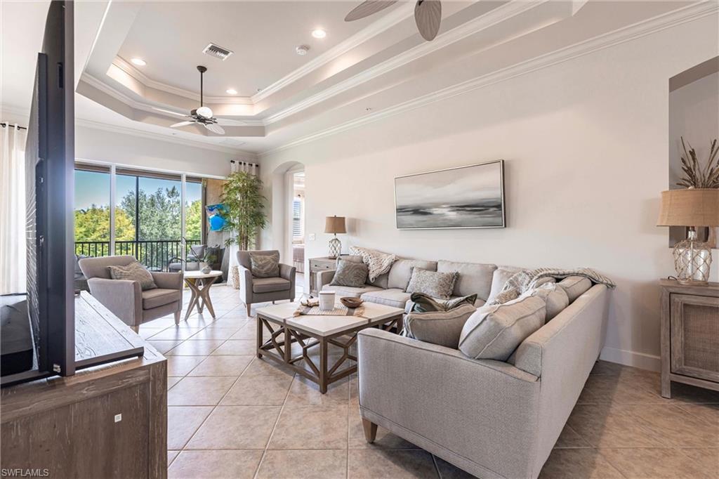 9550 Ironstone Terrace, Unit 201 Naples, FL 34120 - Photo 6 of 50 Living room with ceiling fan, a tray ceiling, crown molding, light tile patterned floors, and arched walkways