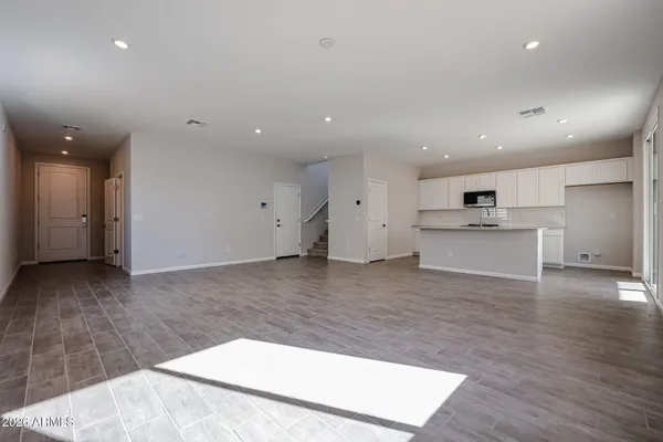 a view of an empty room with wooden floor kitchen view and a window